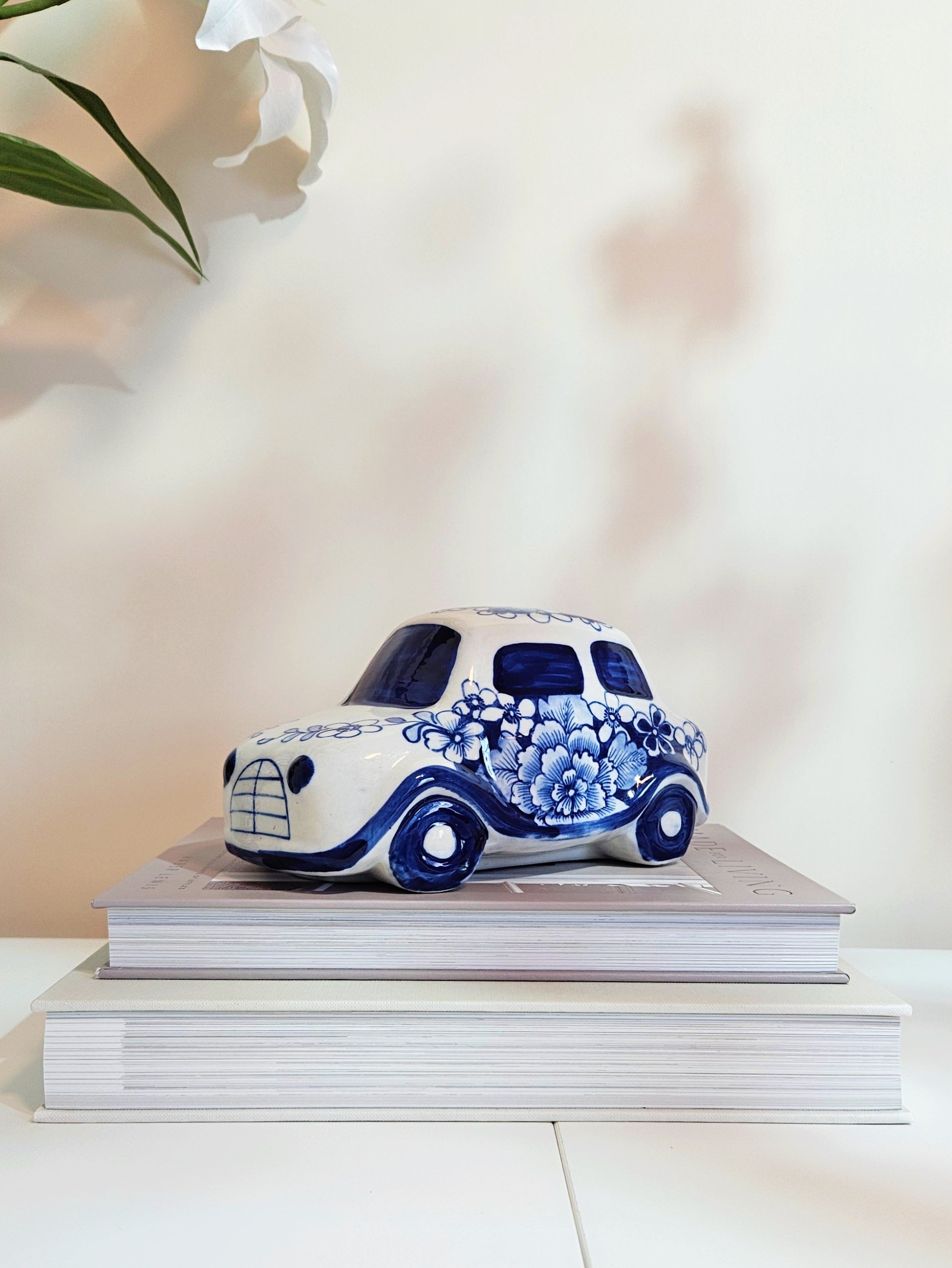 A blue and white chinoiserie ceramic car figurine with floral motif placing on two stacked books in beige background
