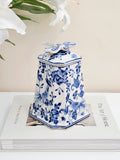 A blue and white porcelain jar with dragonfly lid featuring floral and bird patterns, displayed on top of a white book with white lilies in the background.