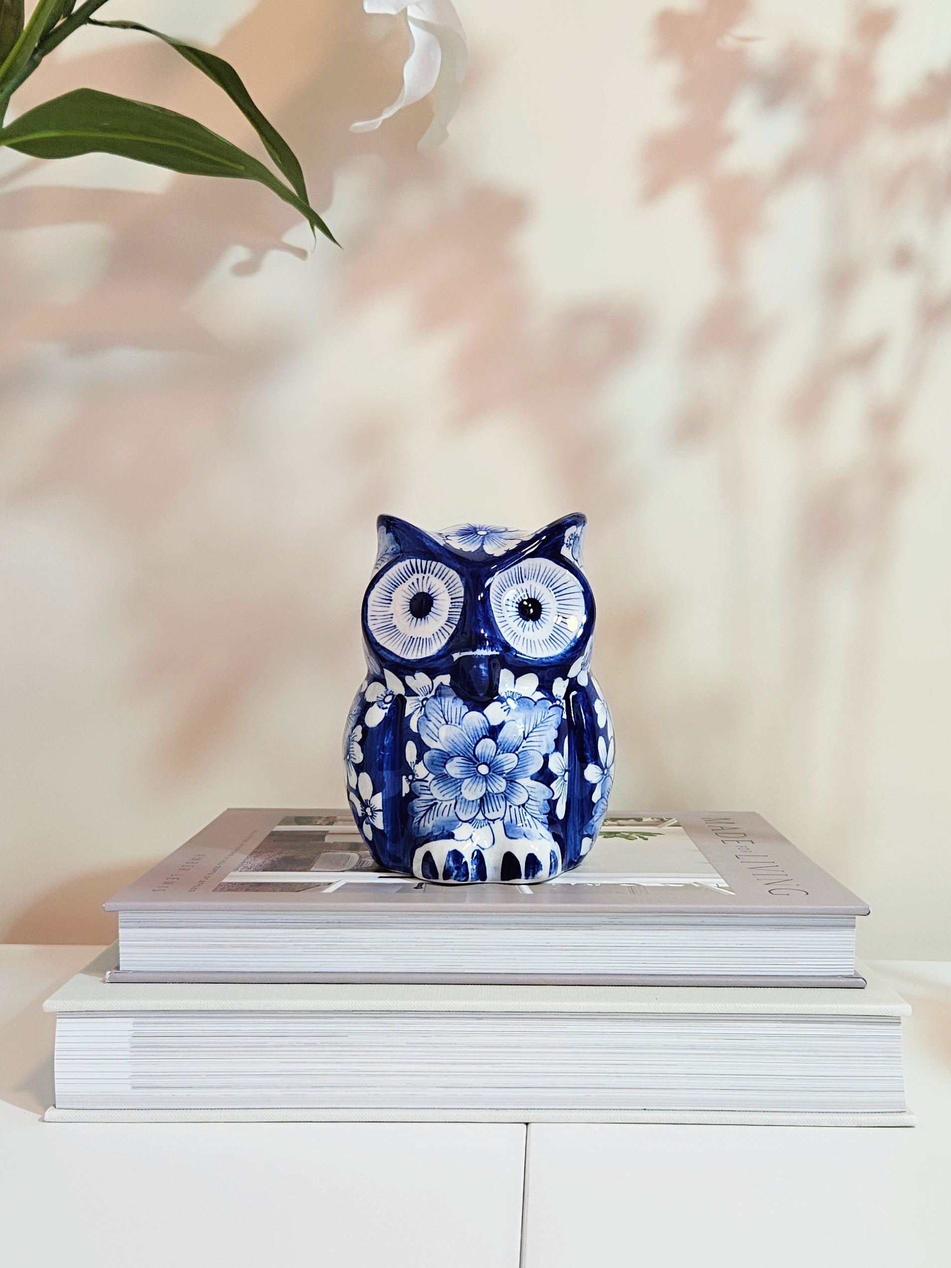 Hand-painted chinoiserie blue and white porcelain owl figurine standing on stacked books with beige background behind