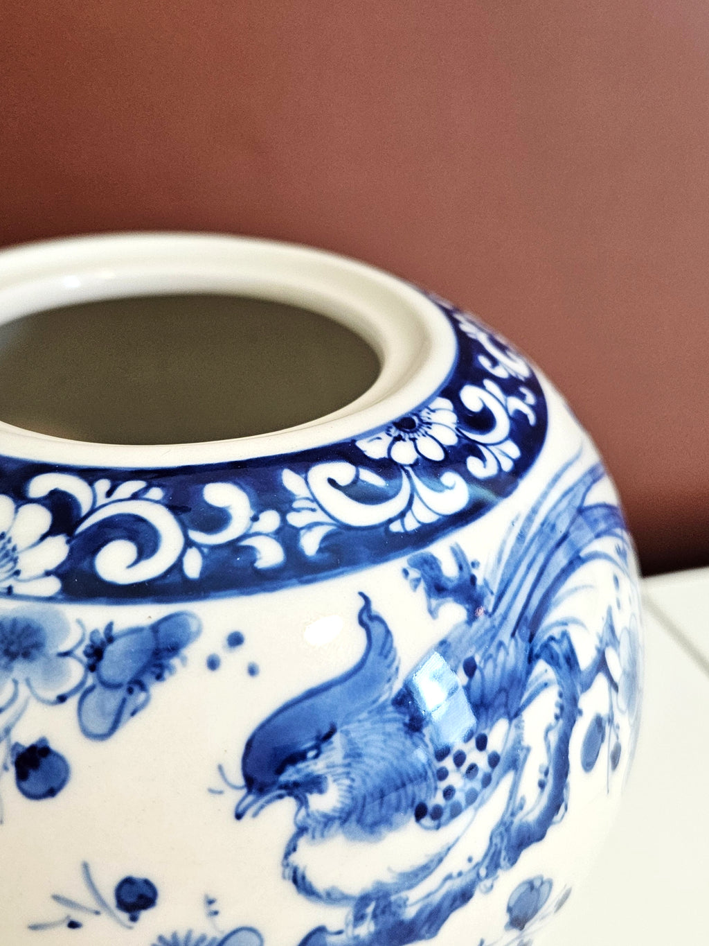 Close-up of a white ceramic jar decorated with blue floral and bird motifs, set against a warm brown background.