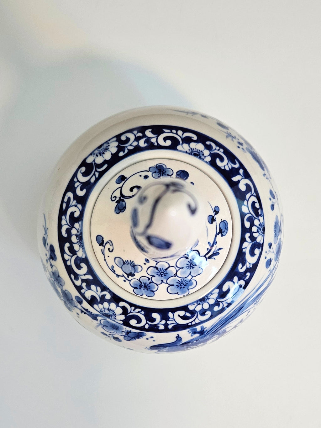 A top-down view of a round ceramic lidded container or vase with a blue and white floral pattern on a light background.