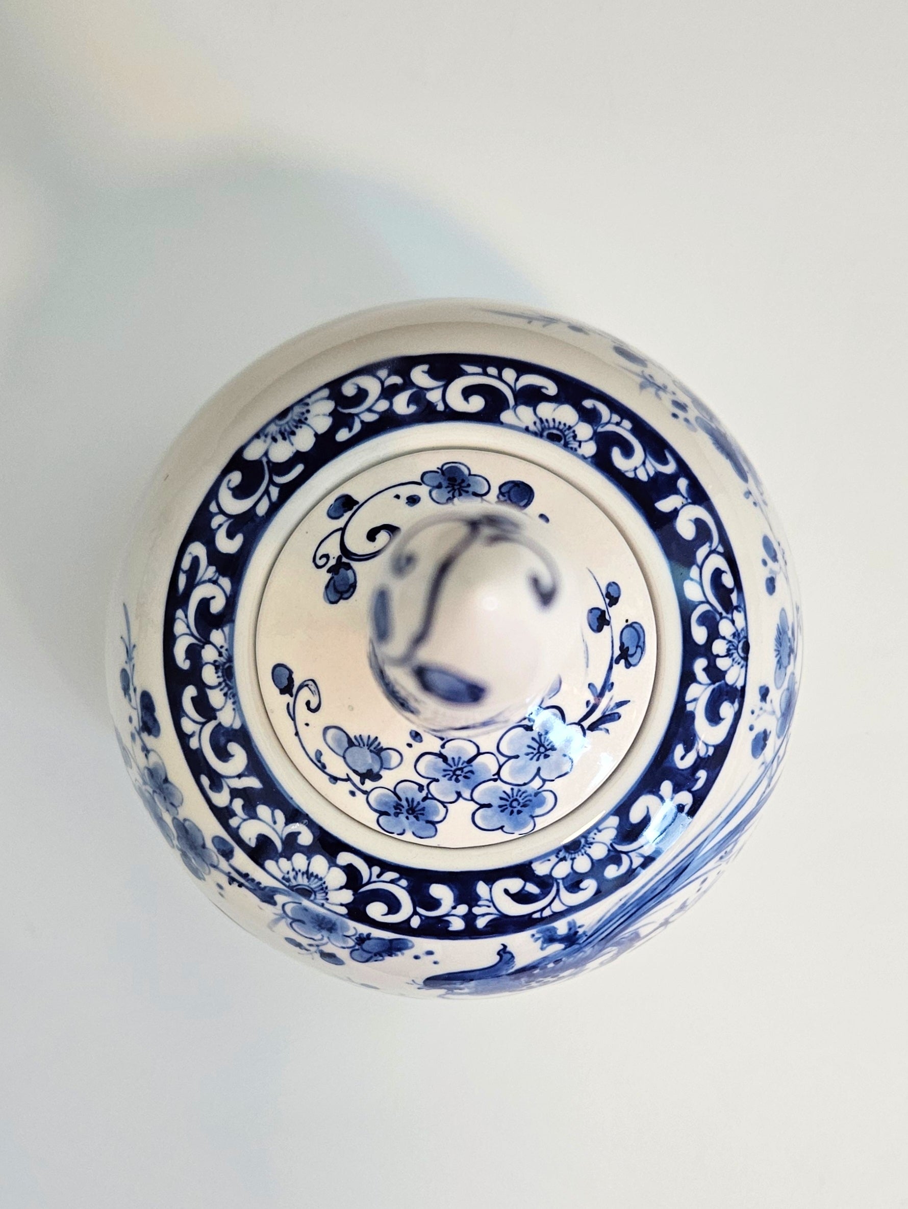 A top-down view of a round ceramic lidded container or vase with a blue and white floral pattern on a light background.