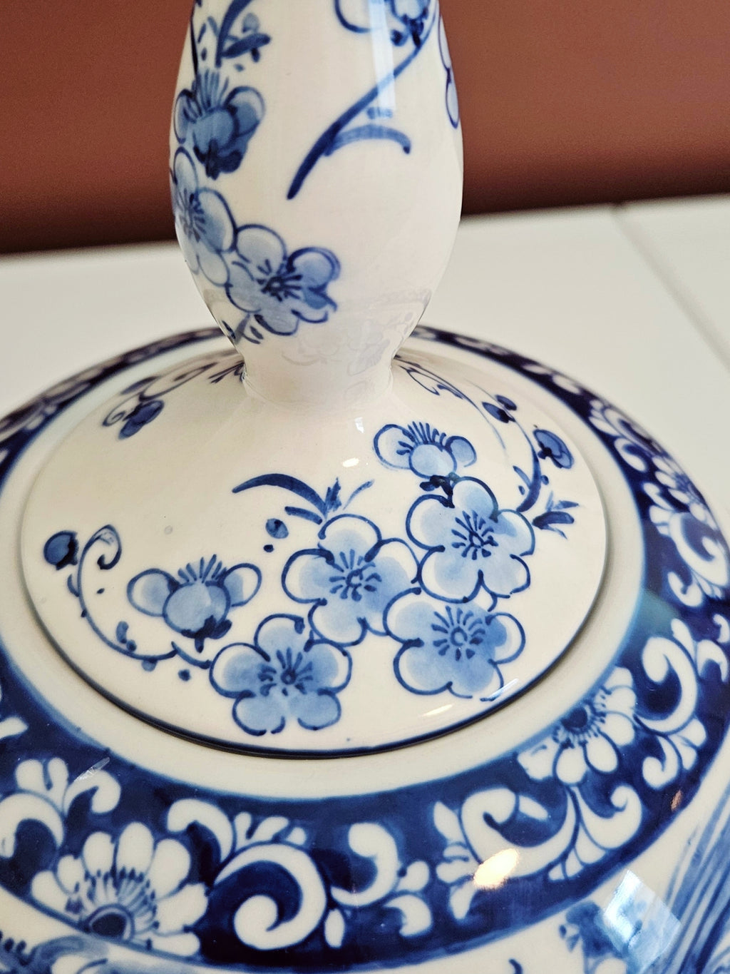 Close-up of a white ceramic jar with a matching lid, decorated with blue floral and scroll patterns.