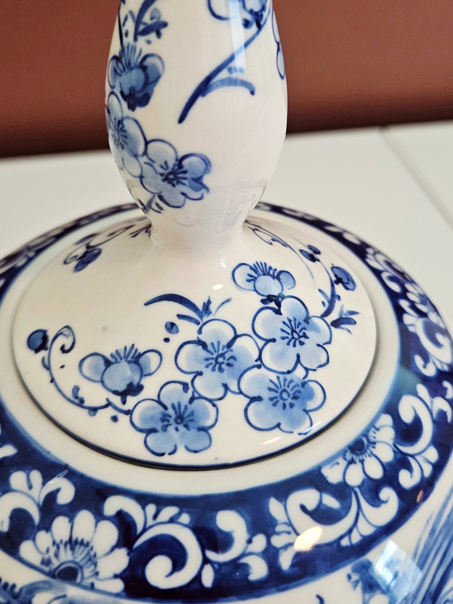 Close-up of a white ceramic jar with a matching lid, decorated with blue floral and scroll patterns.