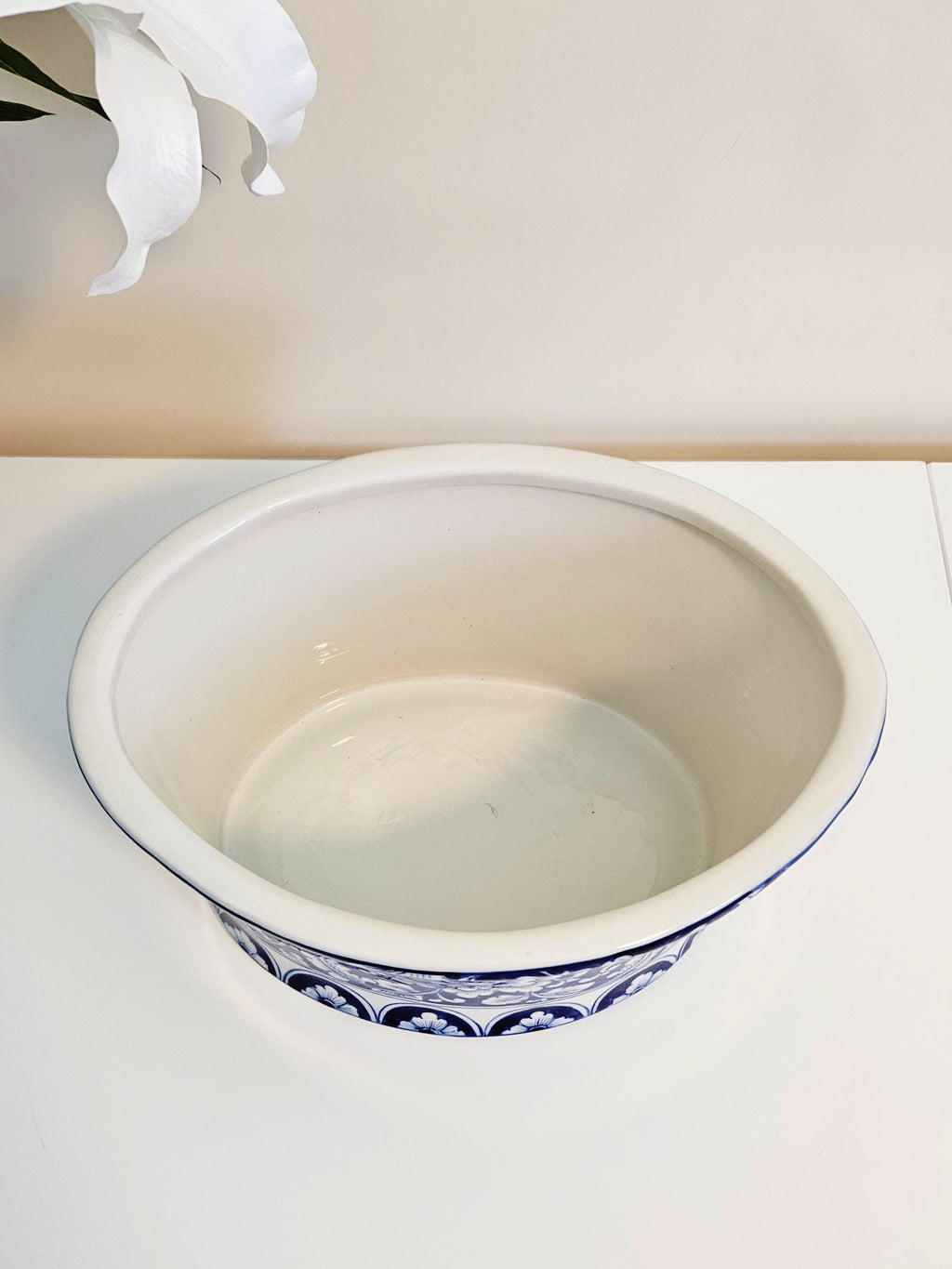 A white ceramic bowl with a blue floral pattern around the base, shown on a white surface against a beige wall.