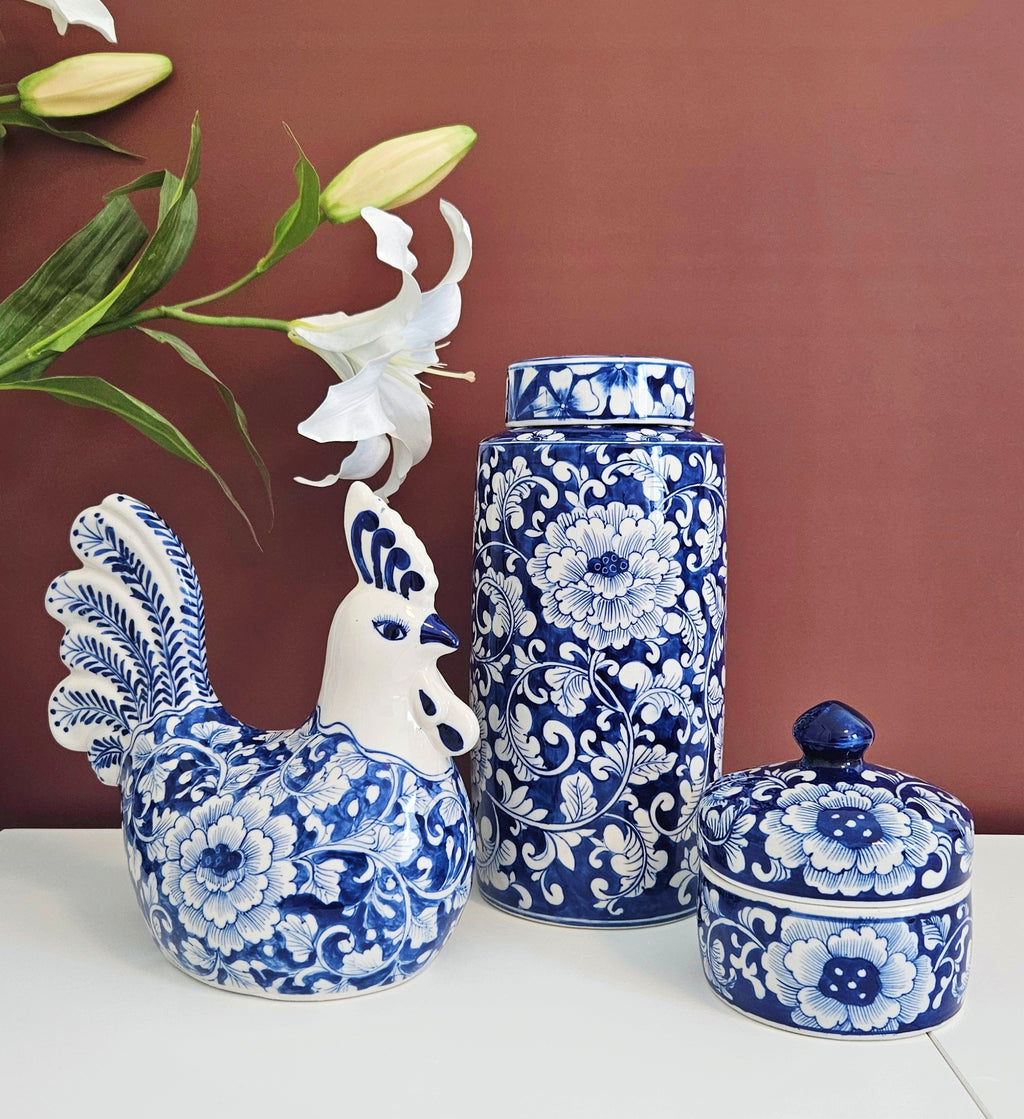 a chinoiserie blue and white porcelain lidded jar standing next to the blue and white porcelain rooster and small storage jar with the same floral vine motif.