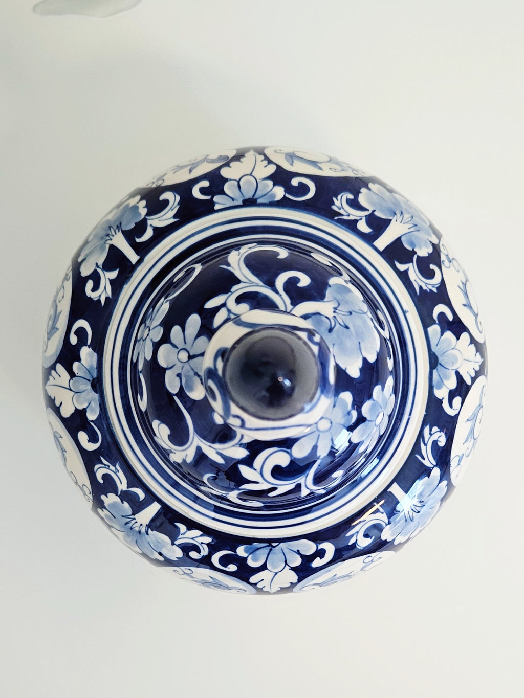 A top-down view of a round blue and white patterned ceramic lidded jar or decorative canister with a central knob, set against a plain light background.