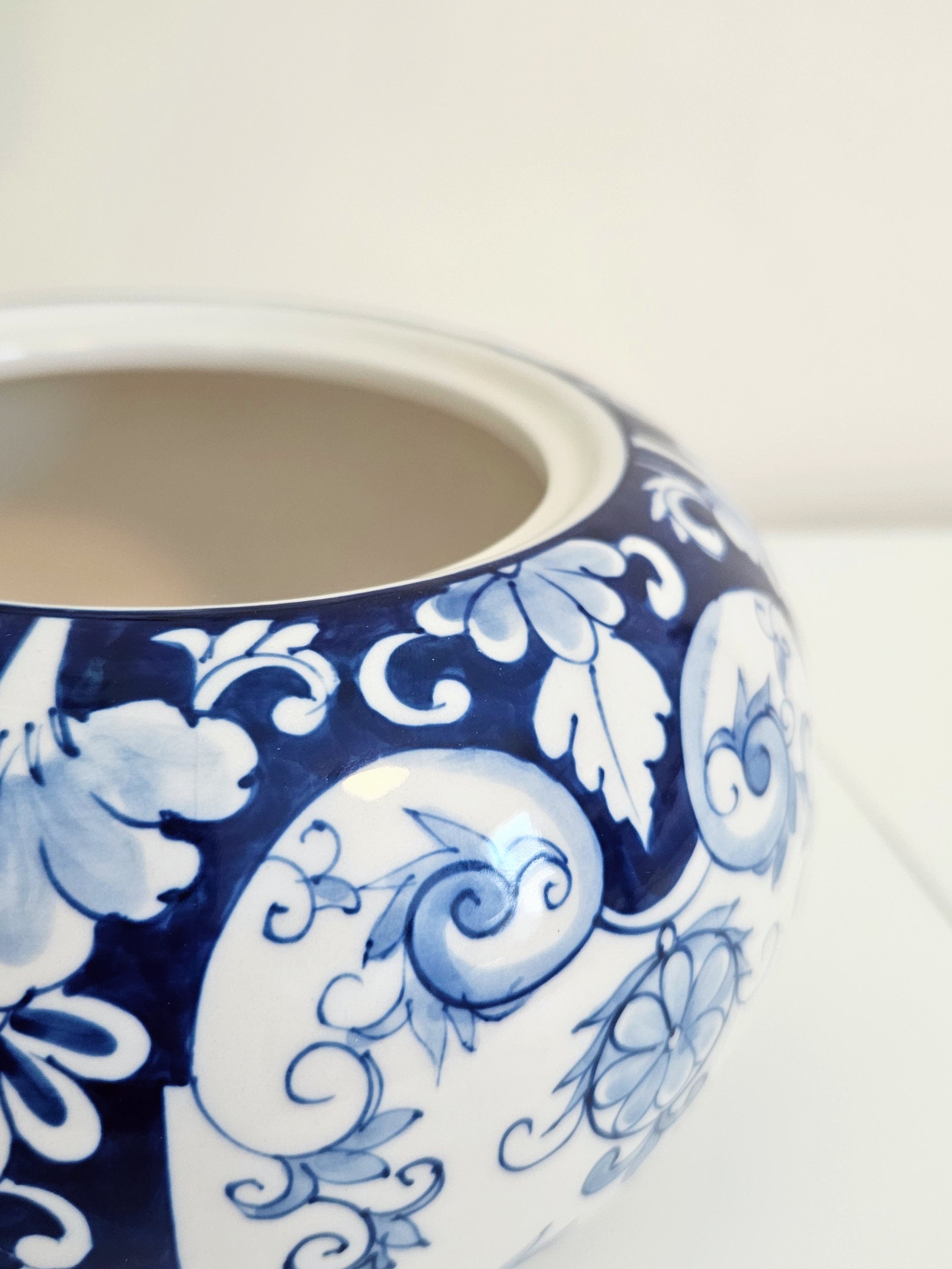 Close-up of a chinoiserie ceramic lidded jar/ canister with a blue and white floral scroll pattern, showing the interior glaze and part of the base on a light surface.