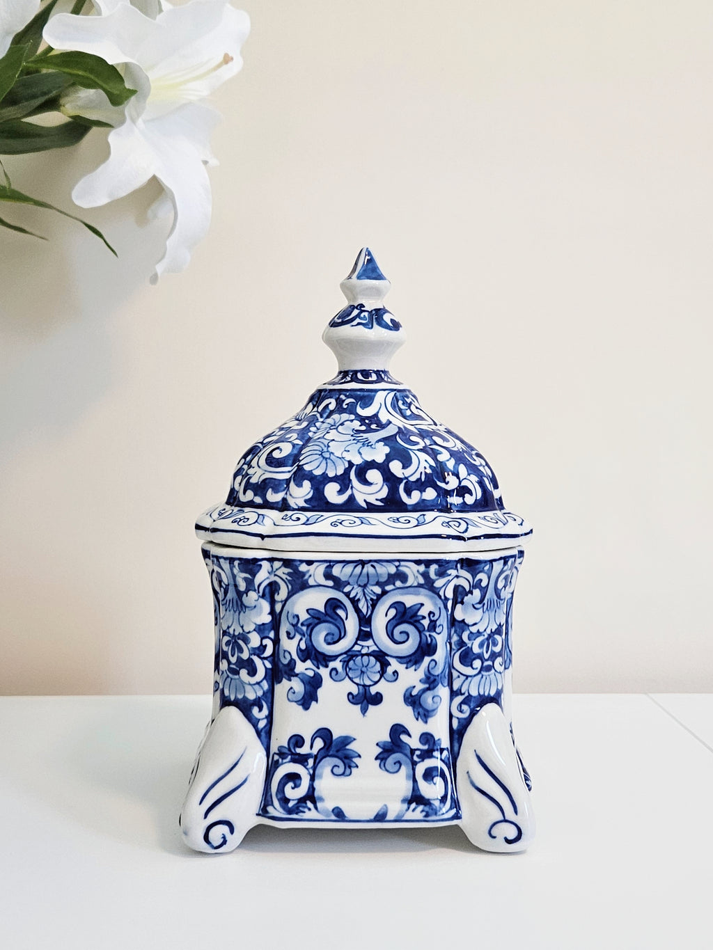A hand-painted chinoiserie blue and white porcelain jar with lid displaying on a white surface with beige background