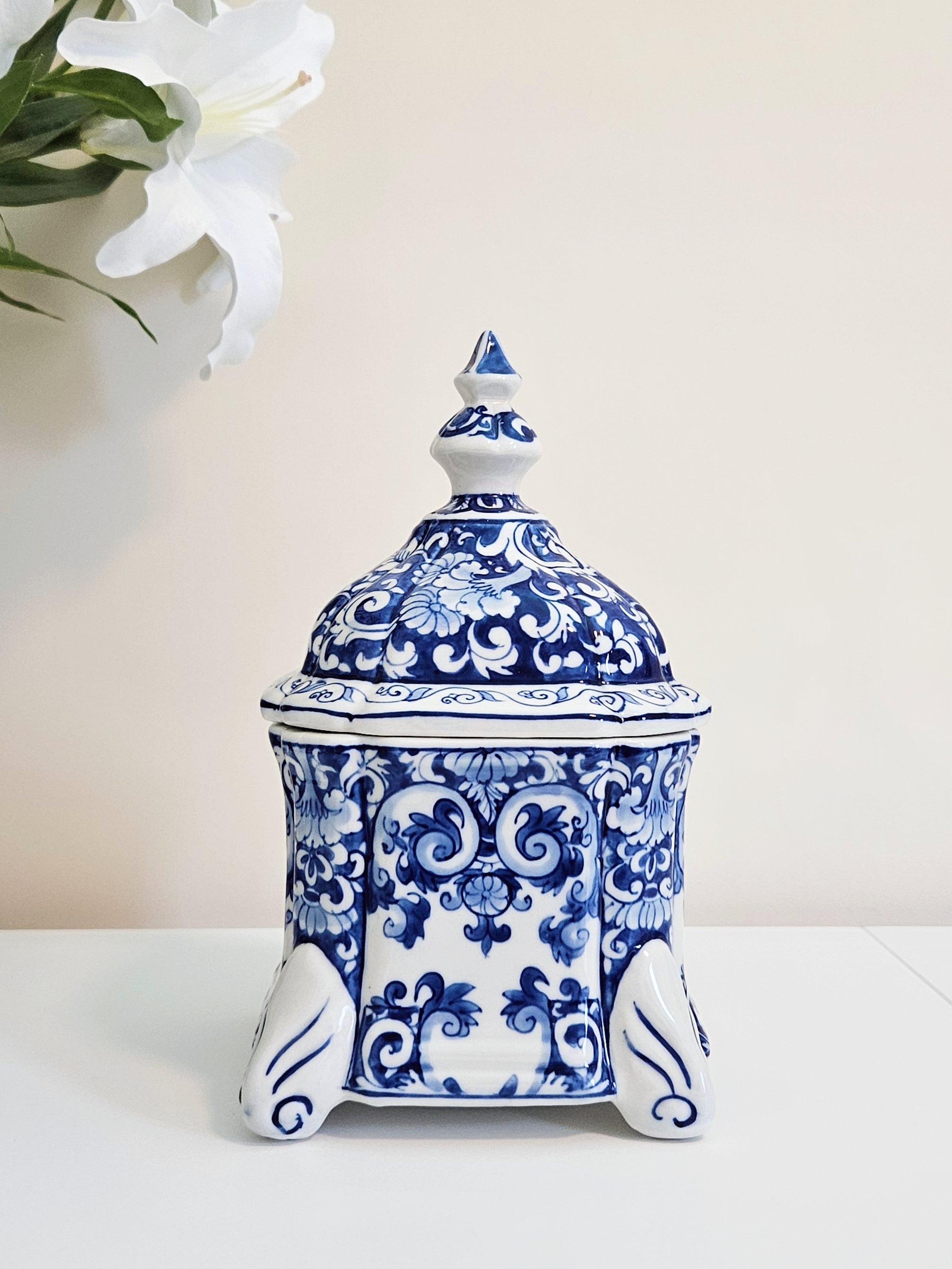 A hand-painted chinoiserie blue and white porcelain jar with lid displaying on a white surface with beige background