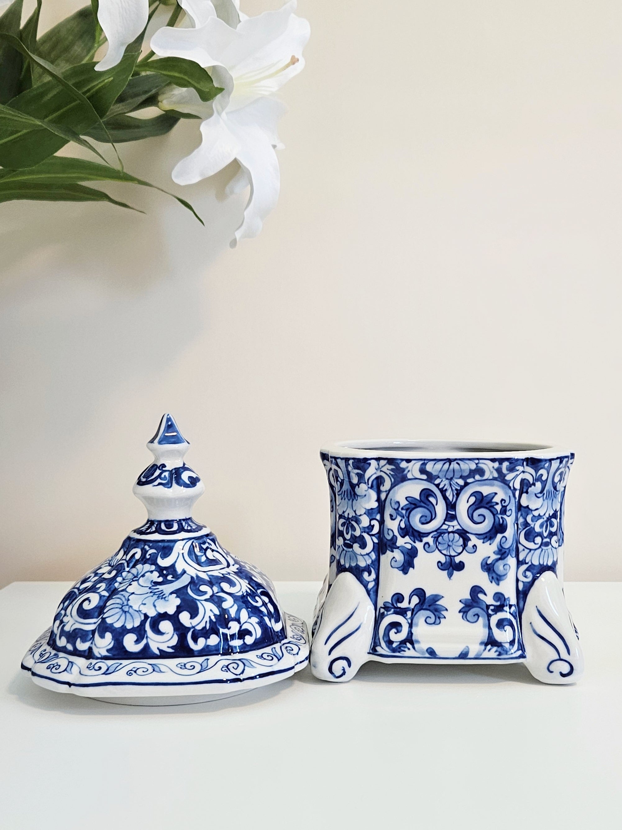 a blue and white porcelain canister with removable lid, display on a white table with lily flower in the background