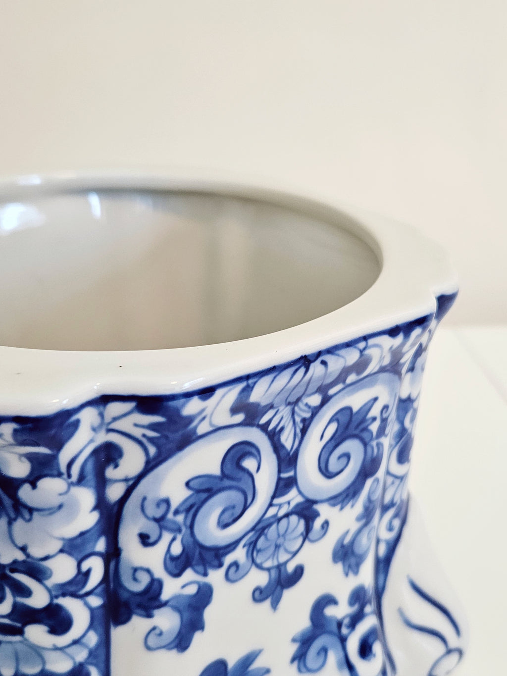 Close-up of a blue and white ceramic jar or canister with a blue floral scroll pattern, showing the interior and part of the exterior on a light background.