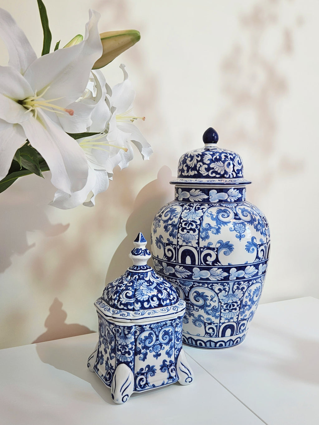 a hand-painted blue and white chinoiserie porcelain jar being displayed next to ceramic temple jar with similar pattern.