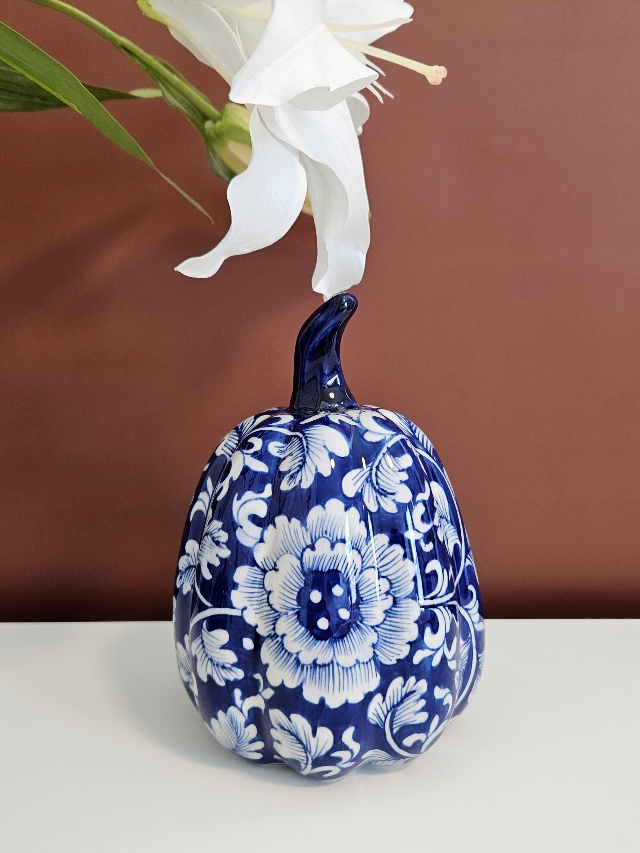 A decorative ceramic pumpkin figurine with a cobalt blue and white floral pattern, set against a solid brown background.