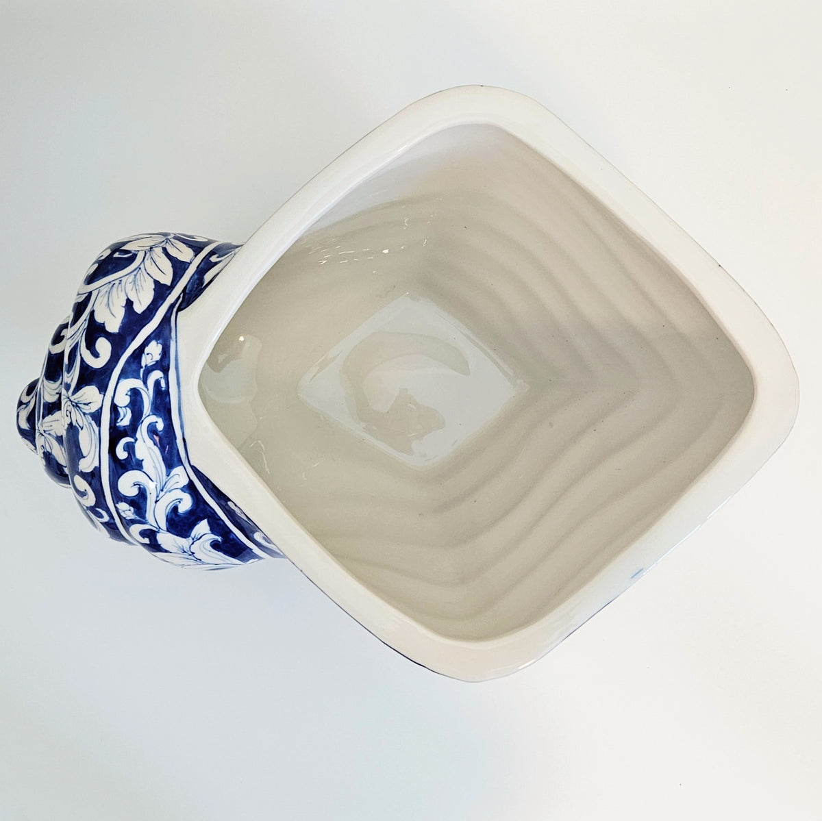 A shell shaped ceramic planter with a wide, shallow interior and a decorative blue and white floral handle, shown from a top-down angle on a white background.