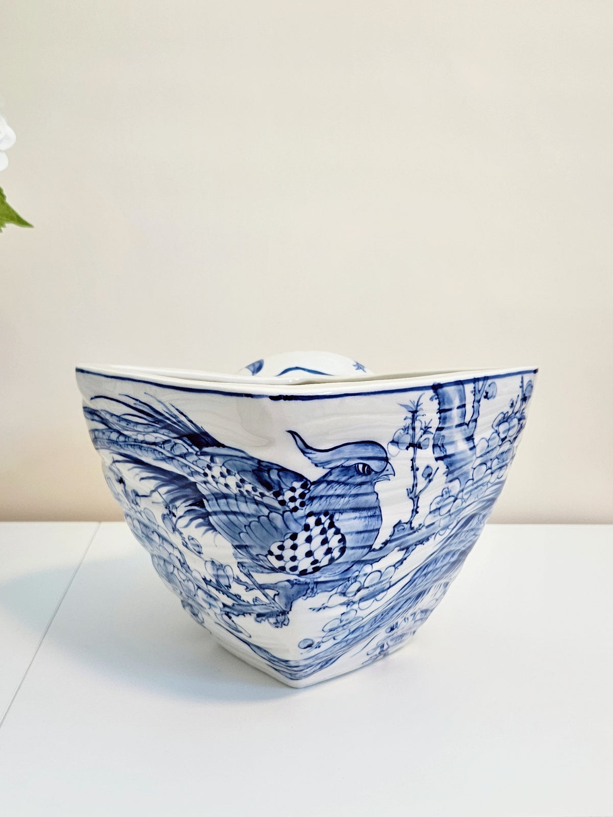 A blue and white ceramic planter pot, decorated with a detailed blue landscape and bird pattern, set against a plain off-white background.