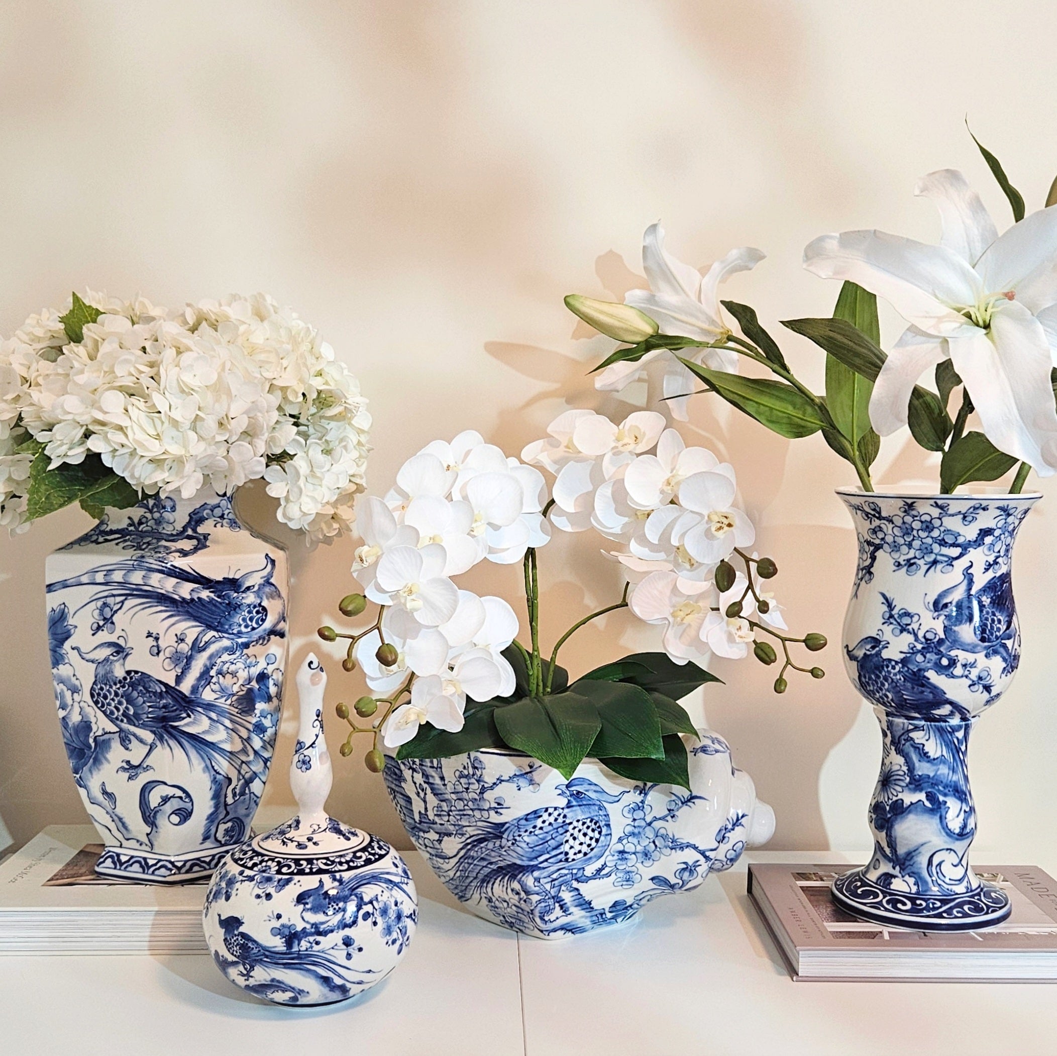 Four blue and white porcelain flower vases with white flowers, arranged on a light surface against a soft beige background.