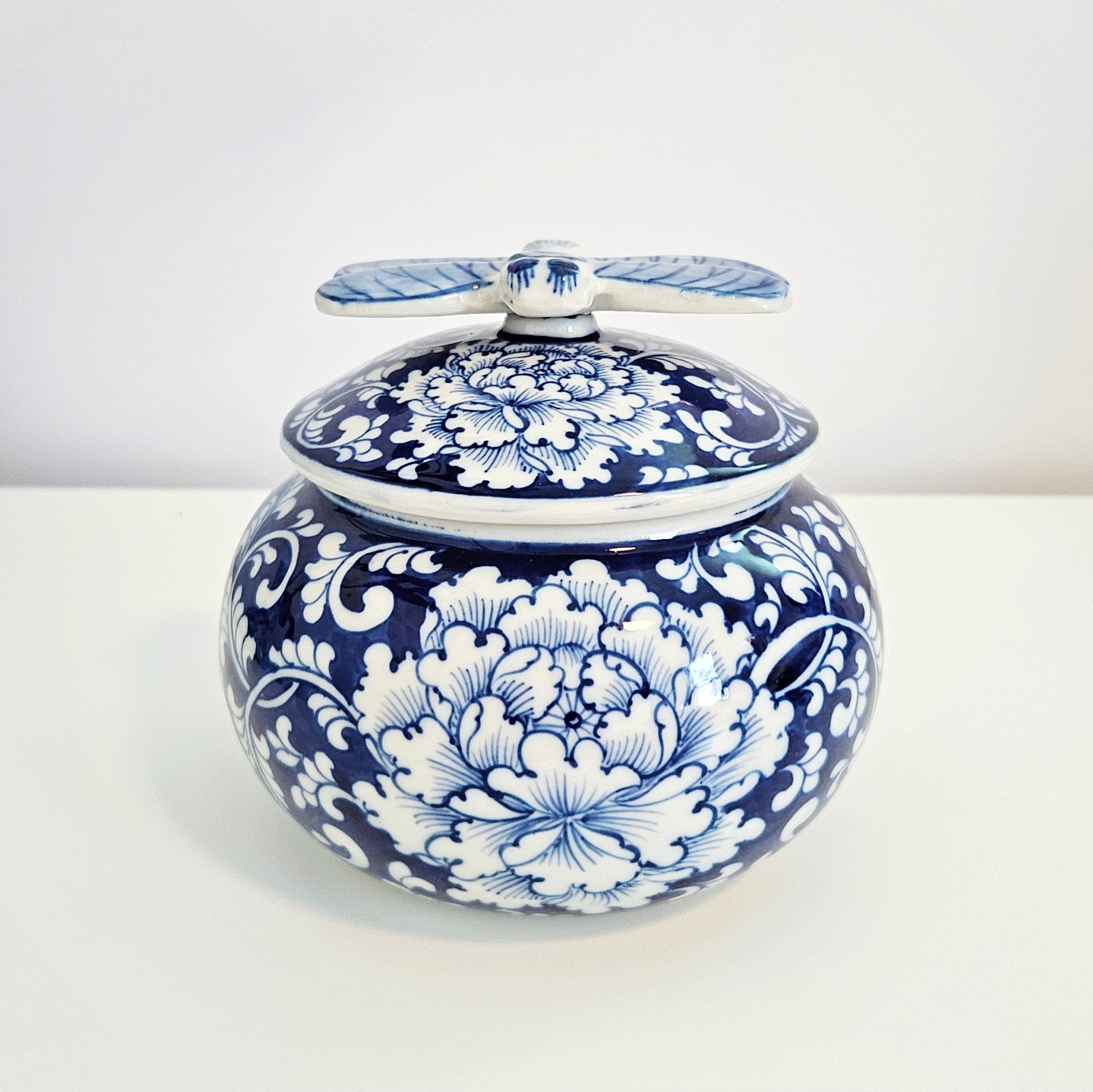 round chinoiserie blue and white porcelain jar with dragonfly lid feature peony flower, placing on a white table